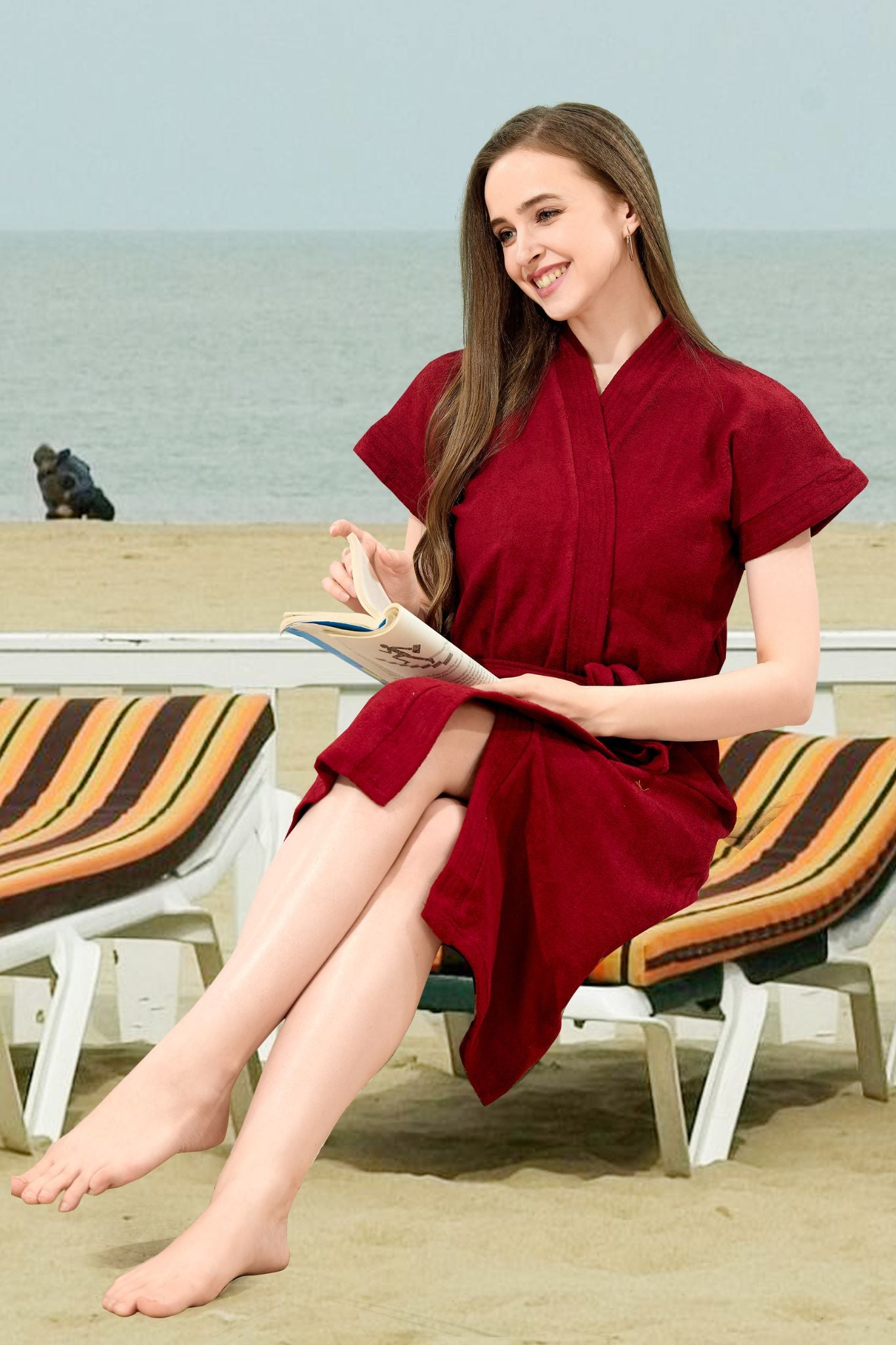 Woman in maroon solid cotton bathrobe reading by the beach